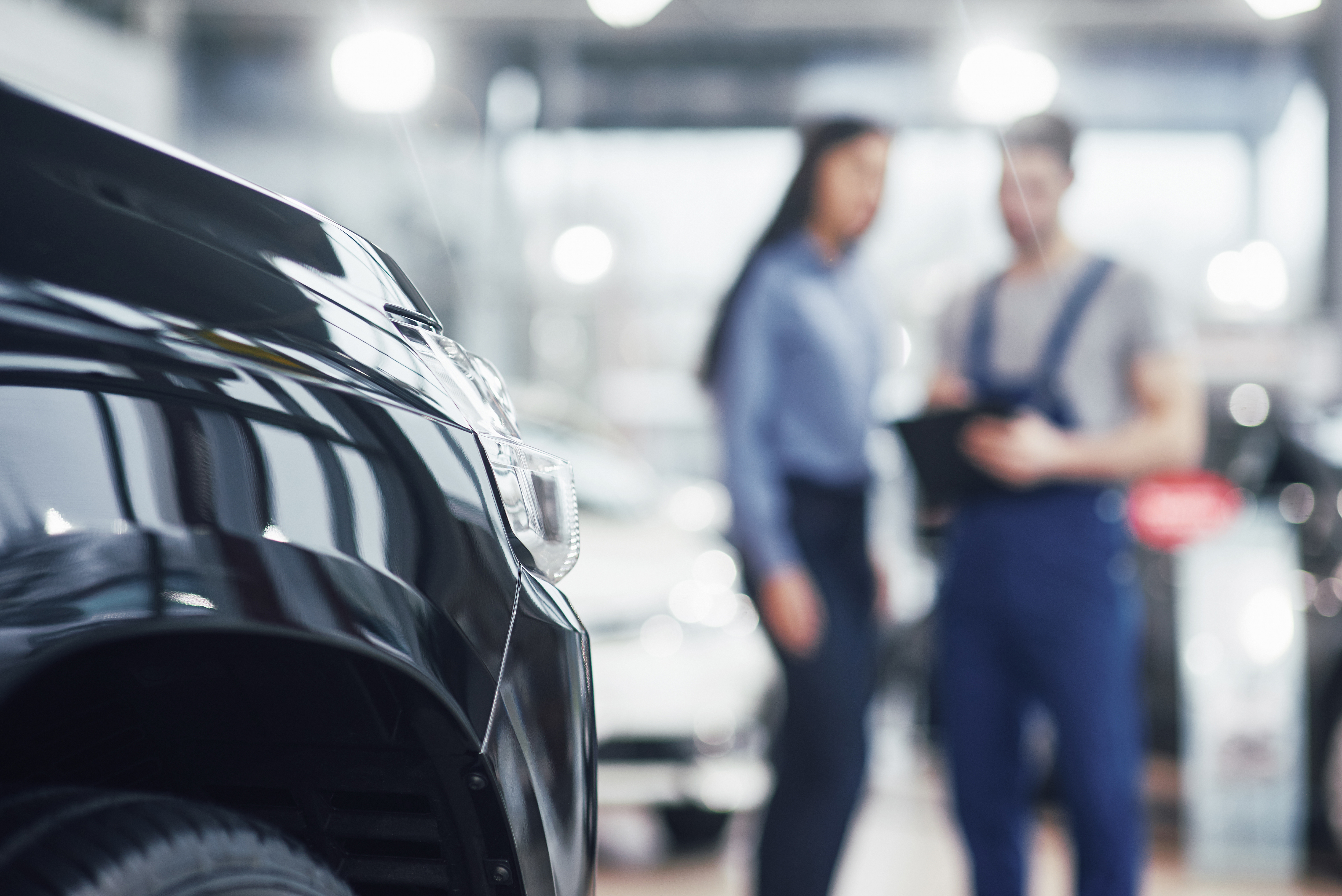 Beautiful young woman is talking to handsome car mechanic while repair a car in dealership Beautiful young woman is talking to handsome car mechanic while repair a car in dealership.